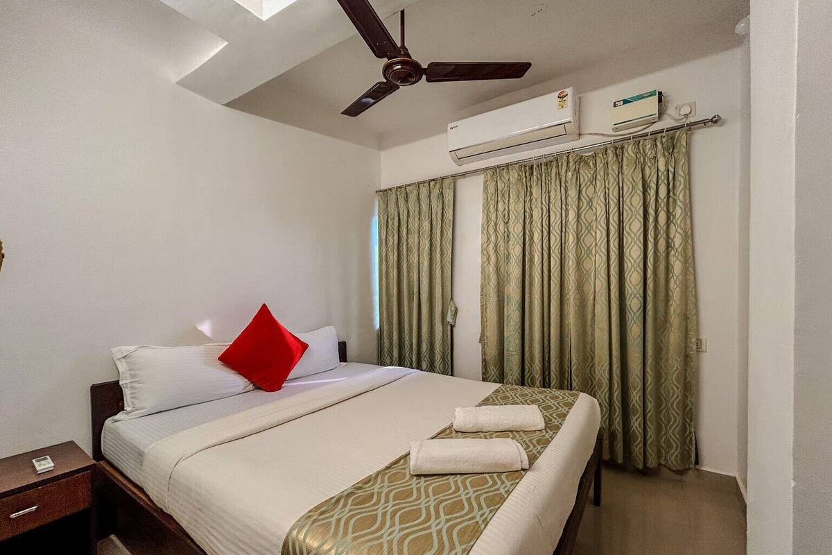 Habitación de hotel con cama, mesita de noche, ventilador de techo, unidad de aire acondicionado y cortinas estampadas.