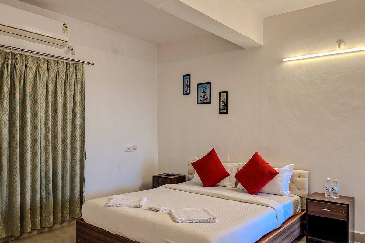 Habitación de hotel con cama, dos mesitas de noche, aire acondicionado de pared y lámpara en el techo.