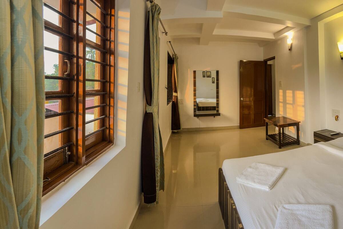 Una habitación de hotel con una cama grande, una mesita de noche, una lámpara de pared y una ventana con cortinas.