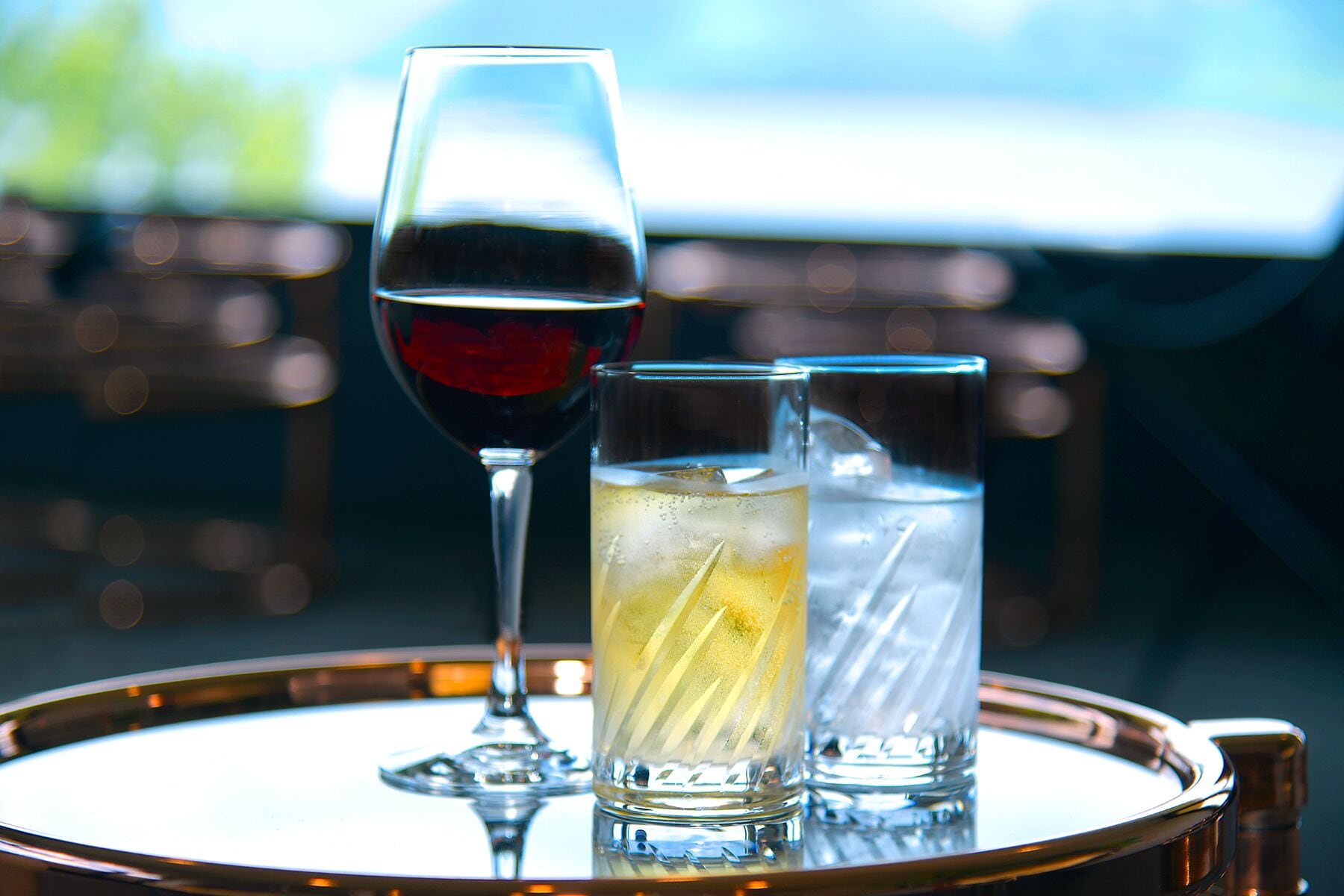 Three glasses on a tray, one with a red liquid, one with a yellow liquid, and one with a clear liquid.