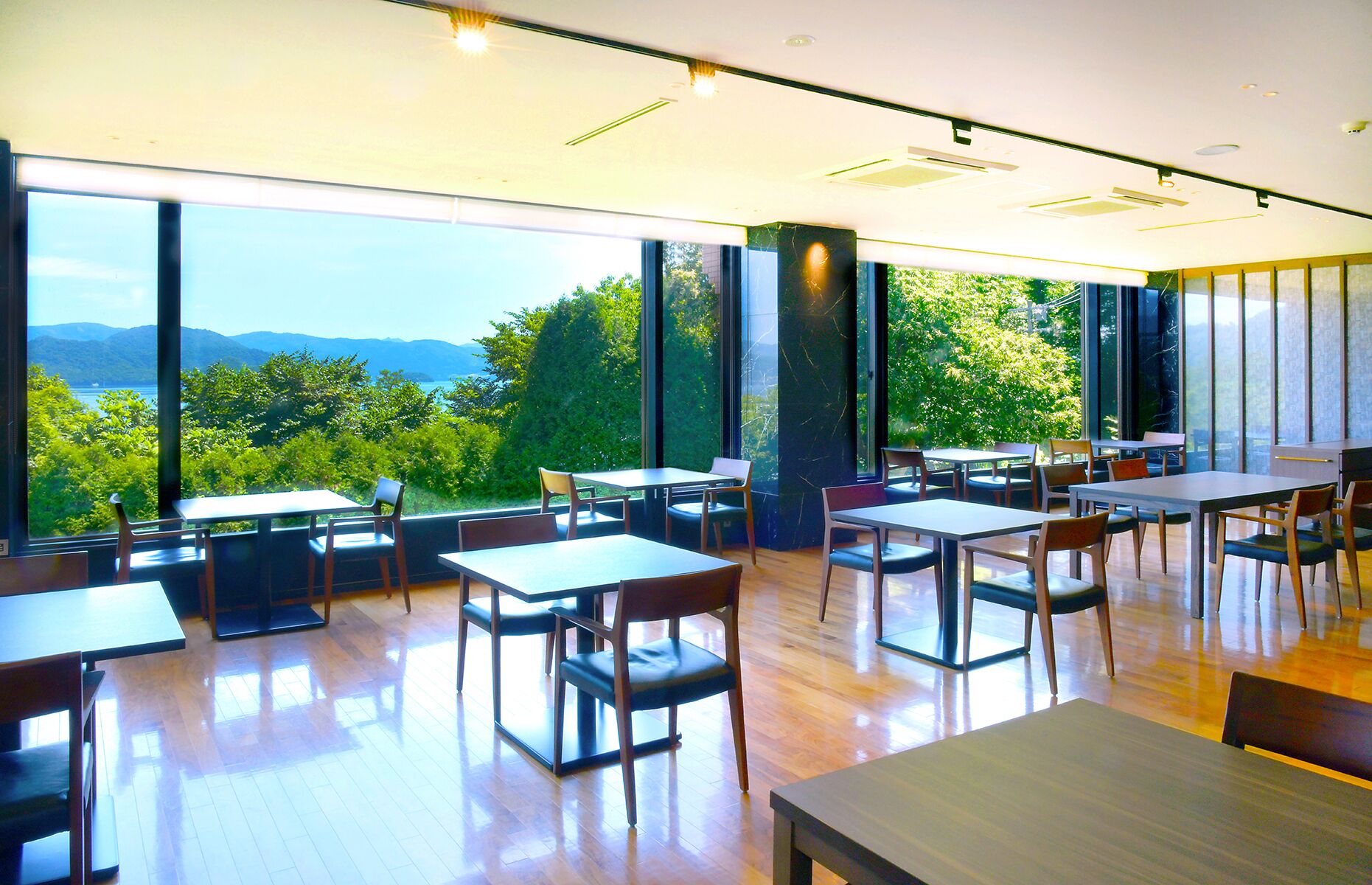 Uma sala de jantar moderna, com grandes janelas que oferecem vista para áreas verdes e montanhas.