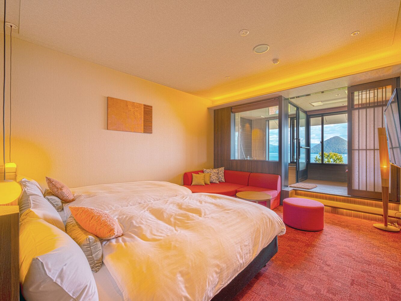 A bedroom with a large bed, a red sofa, a small round table, and a balcony with a view.