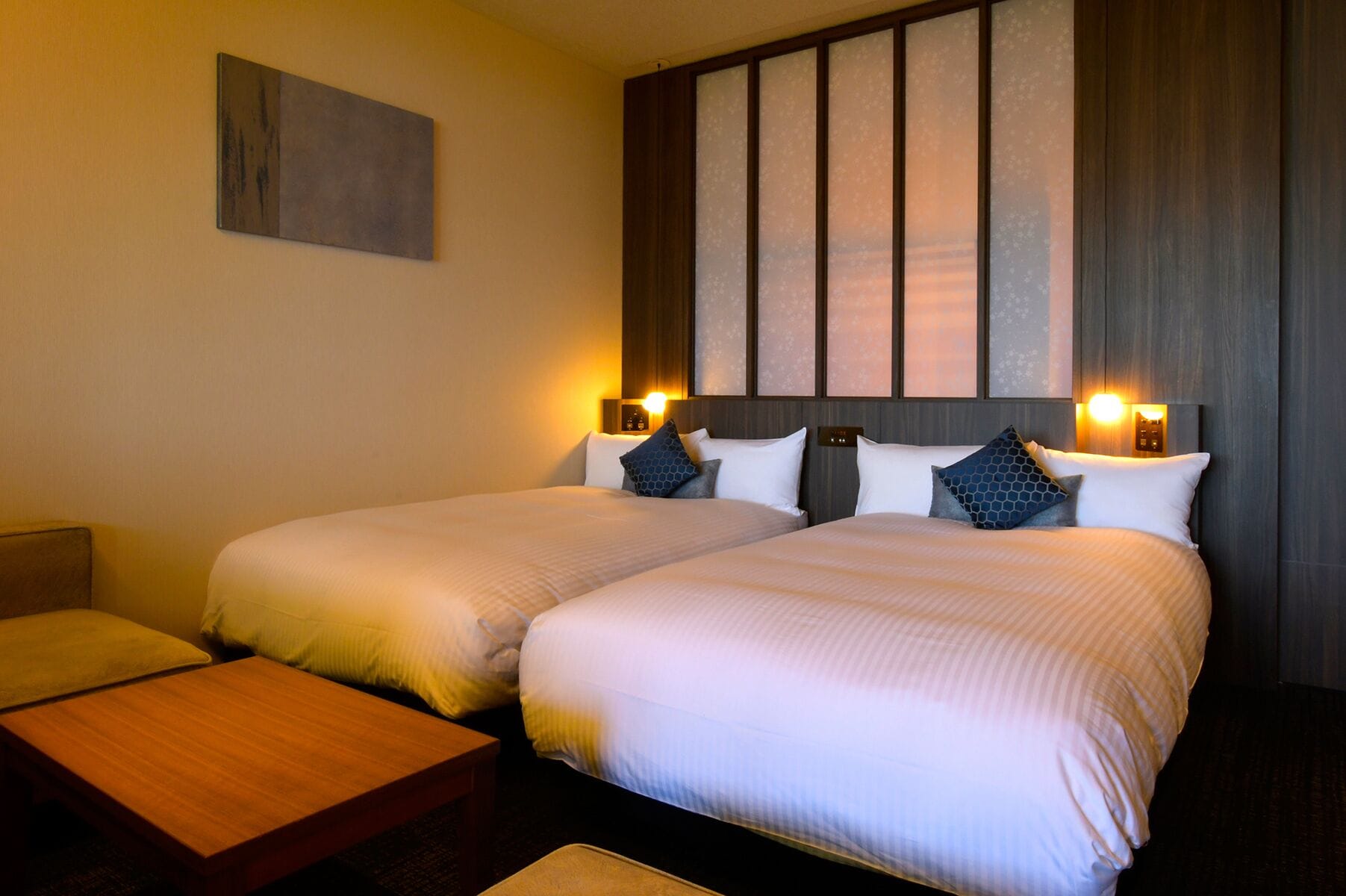 A hotel room with two beds, a small wooden table, and a wall-mounted artwork.
