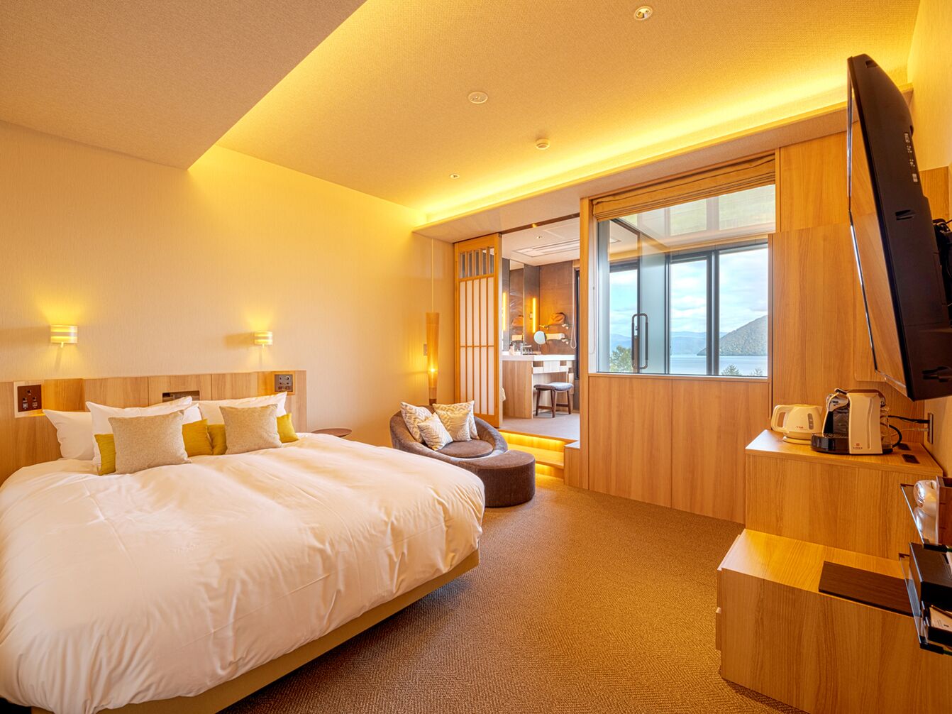 A hotel room with a large bed, a seating area, a television, and a view of the outdoors.