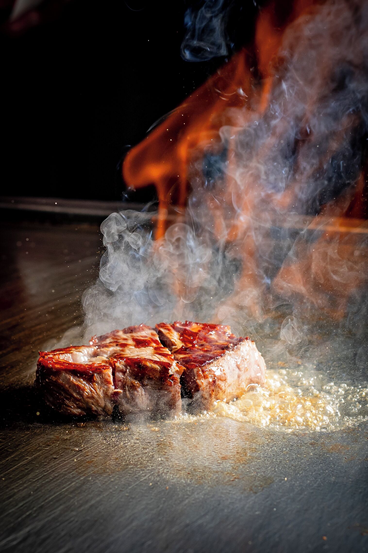 A steak sizzling on a grill with smoke rising.