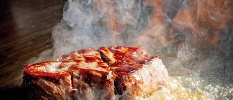 A steak sizzling on a grill with smoke rising.