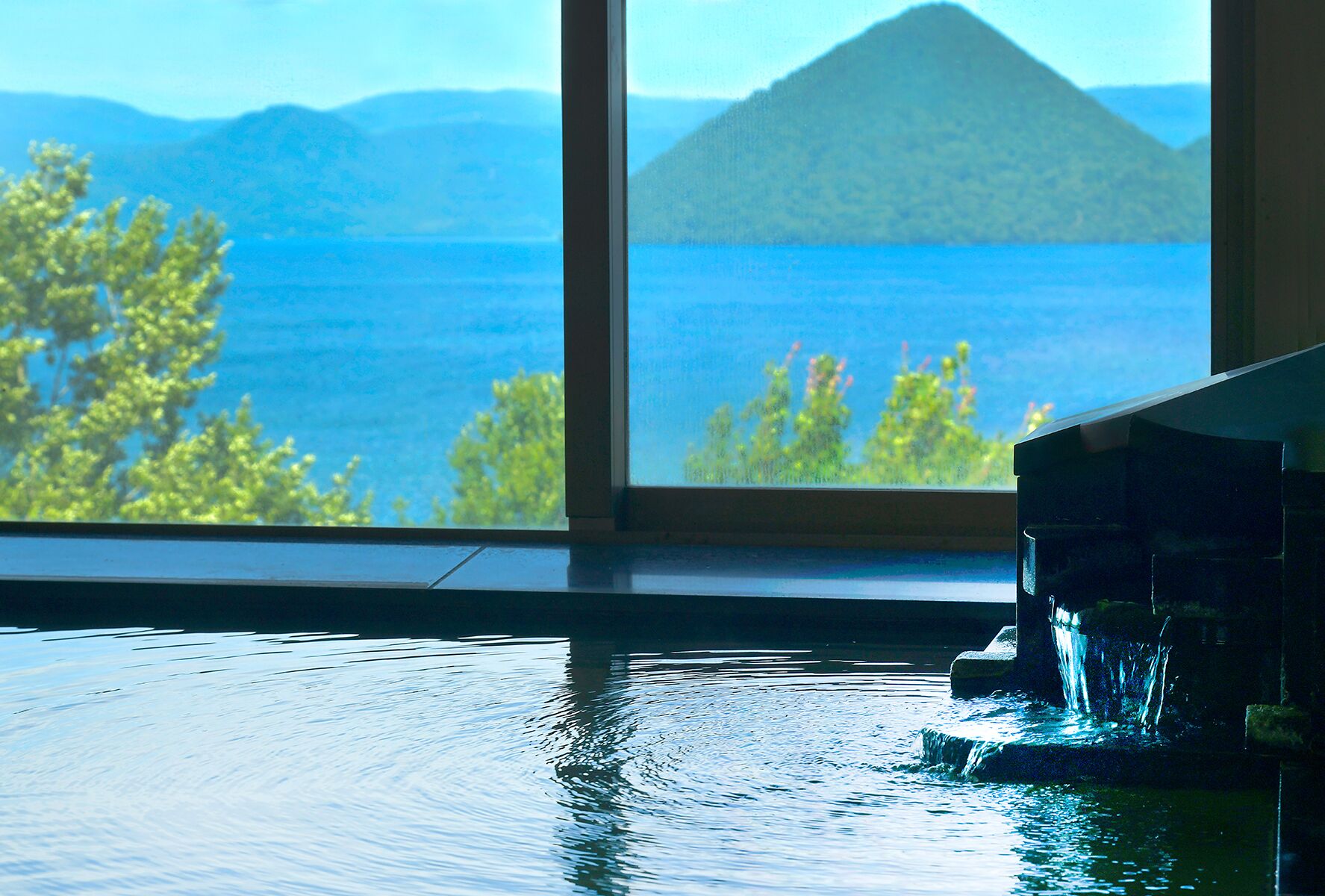 Una habitación con un gran ventanal con vistas a un cuerpo de agua y una montaña.