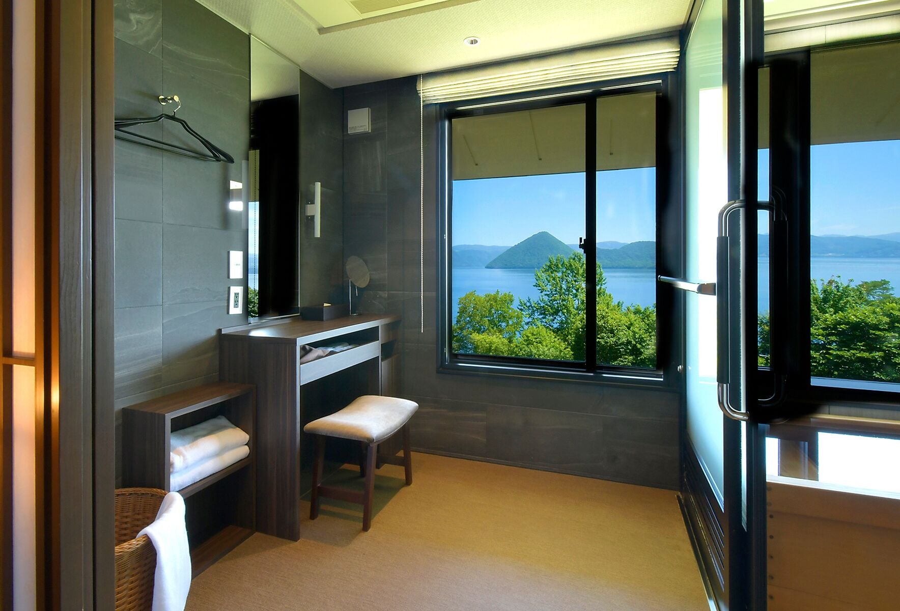 Une salle de bain moderne dotée d’une grande fenêtre, d’un meuble-lavabo, d’un banc et d’un porte-serviettes mural.