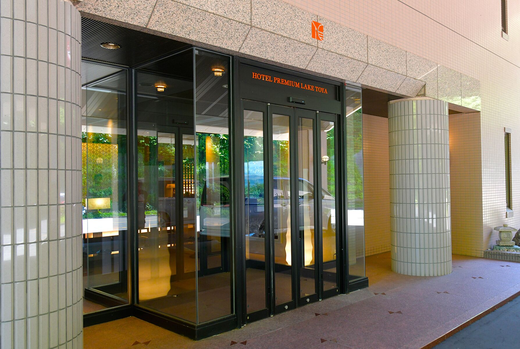 L’entrée de l’hôtel Premium Lake Toya se distingue par une porte en verre et une façade recouverte de carreaux.