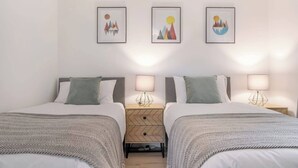 A double room with two beds, a nightstand with a lamp, and three framed artworks on the wall. - Bluebell House - Sleeps 5 - Garden - Parking (Peterborough)