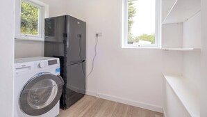 A compact kitchen with a washing machine, a black refrigerator, and a window providing natural light. - Bluebell House - Sleeps 5 - Garden - Parking (Peterborough)