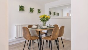 A dining area with a rectangular table set for four, surrounded by six brown upholstered chairs with black legs. - Bluebell House - Sleeps 5 - Garden - Parking (Peterborough)