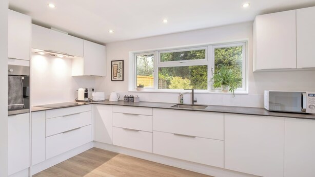 A modern kitchen with white cabinets, a built-in microwave, and a window with a view of greenery. - Bluebell House - Sleeps 5 - Garden - Parking (Peterborough)
