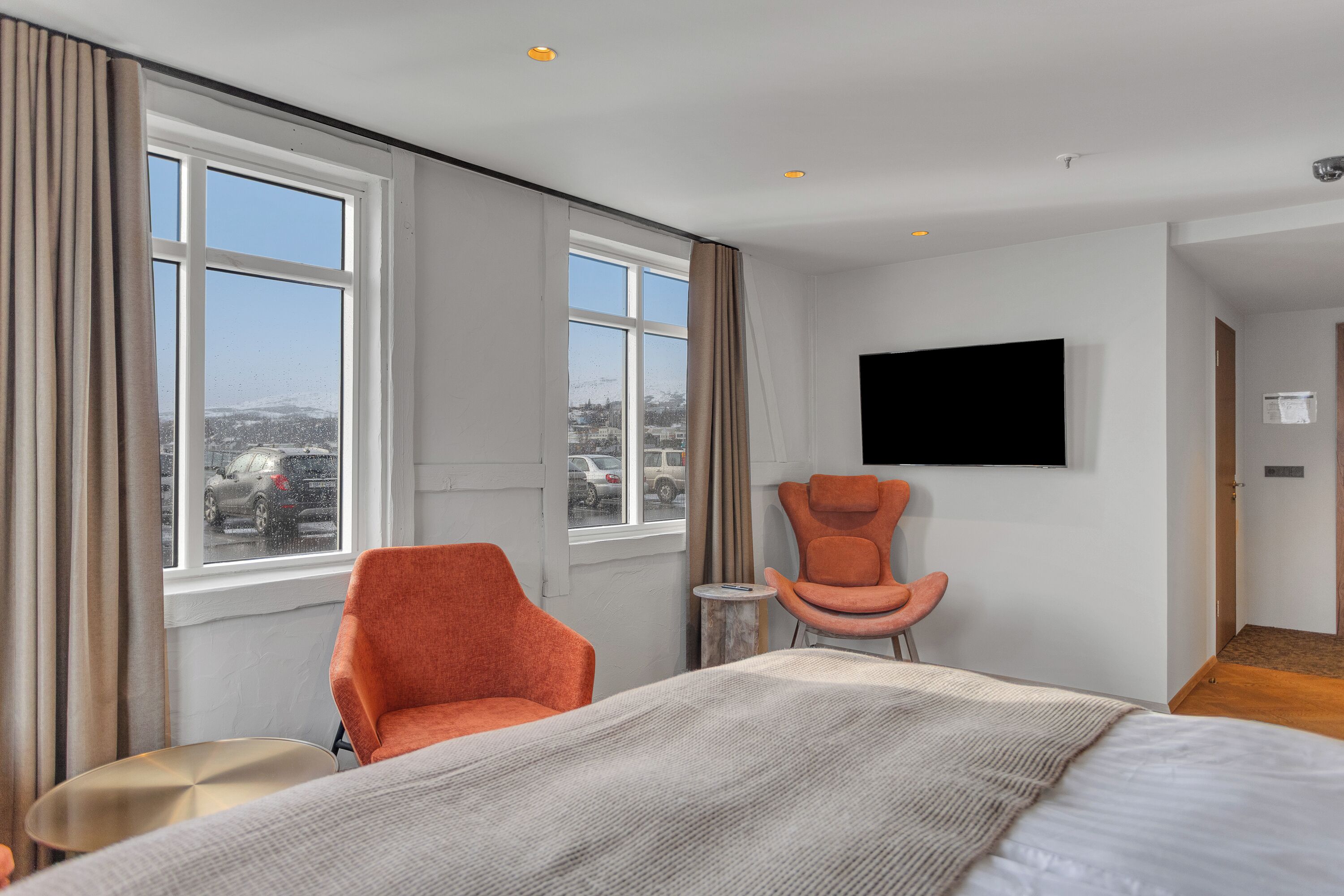 A hotel room with a large bed, two chairs, a TV, and a window with a view of the city.