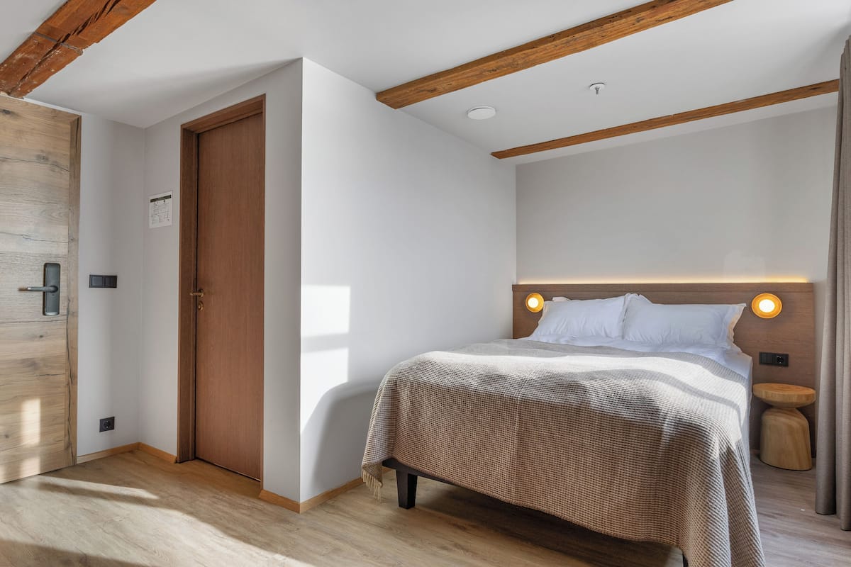 A bedroom with a wooden ceiling, a bed with a headboard, a bedside table, and a door.