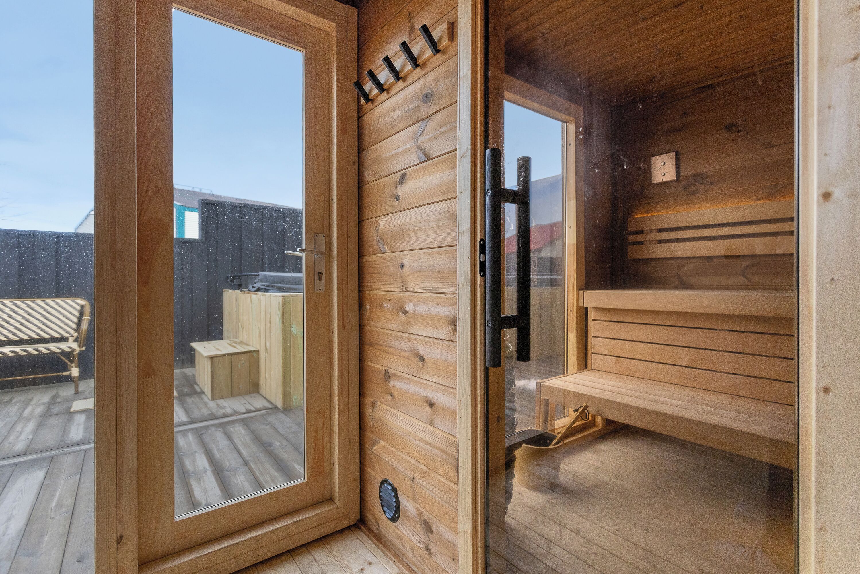 Een sauna met houten wanden en een glazen deur, een bank en een bank met een handdoekhouder.