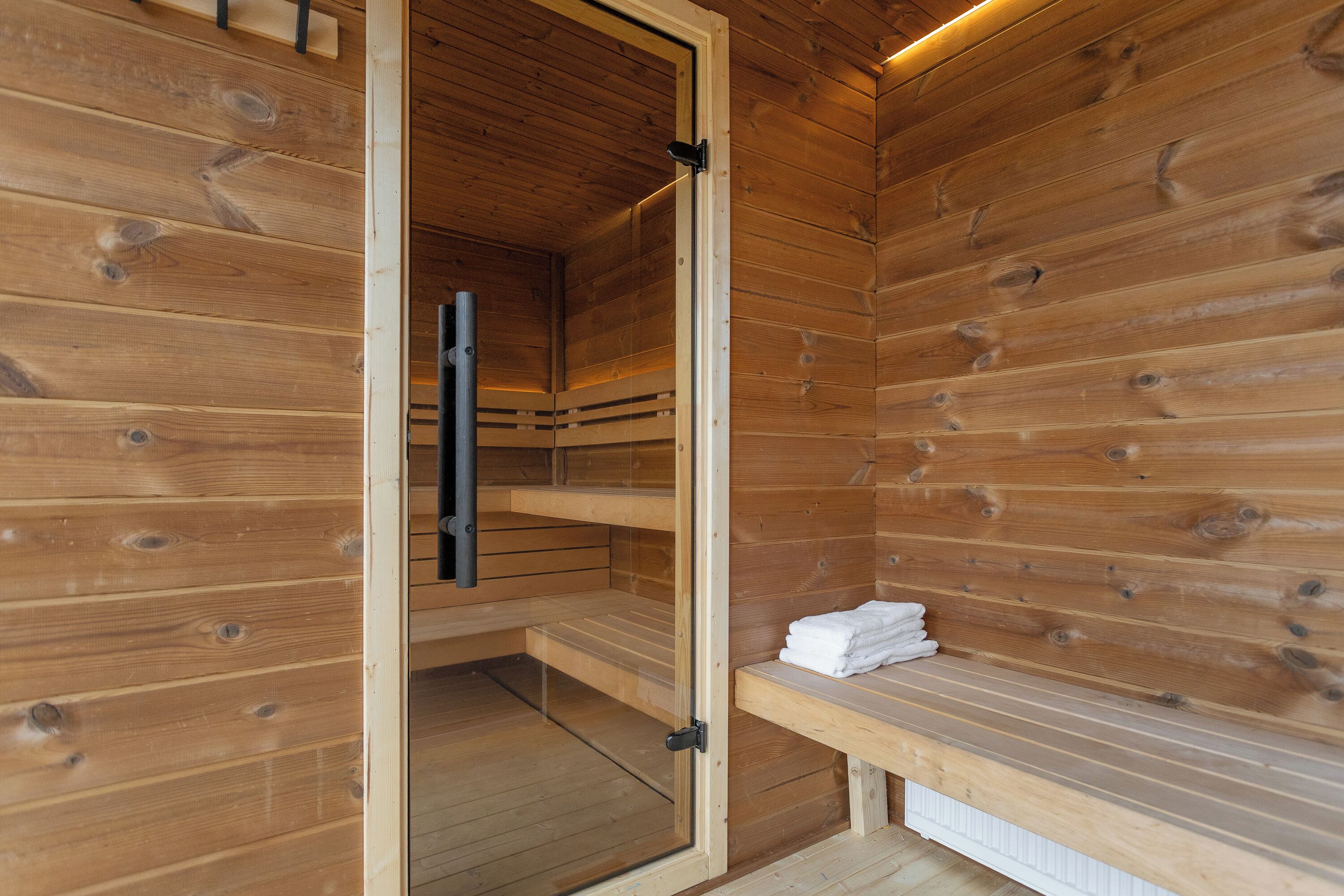 A wooden sauna room with benches and a bench with towels.