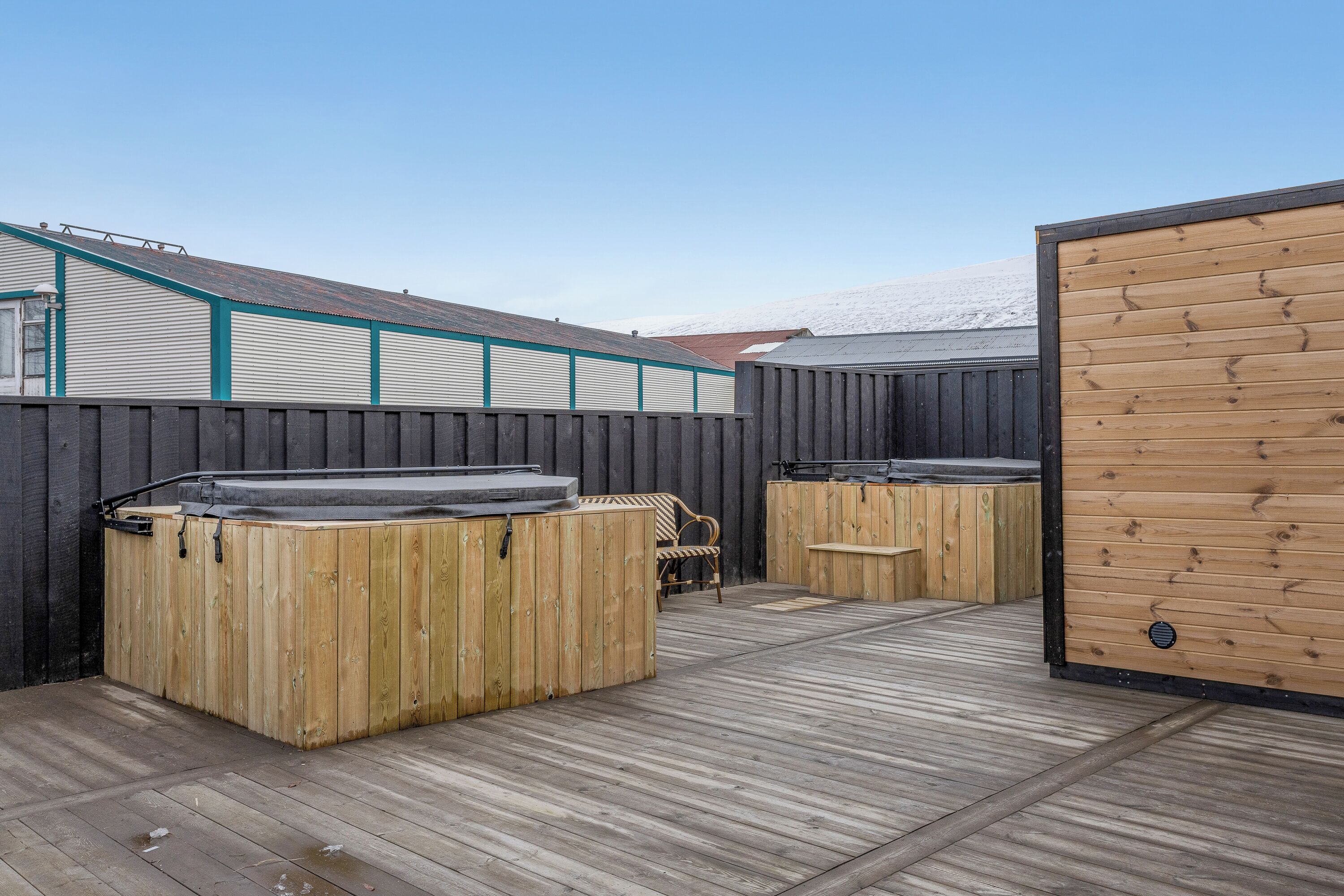 A wooden deck with two hot tubs, a wooden fence, and a building with a metal roof.