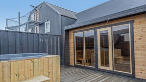 A wooden deck with a hot tub, a sliding glass door, and a metal fence. - Bryggjan Boutique Hotel (Akureyri)
