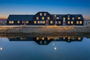 Un edifici gran i fosc amb diverses finestres i una porta vermella, reflectit en una calma massa d'aigua.