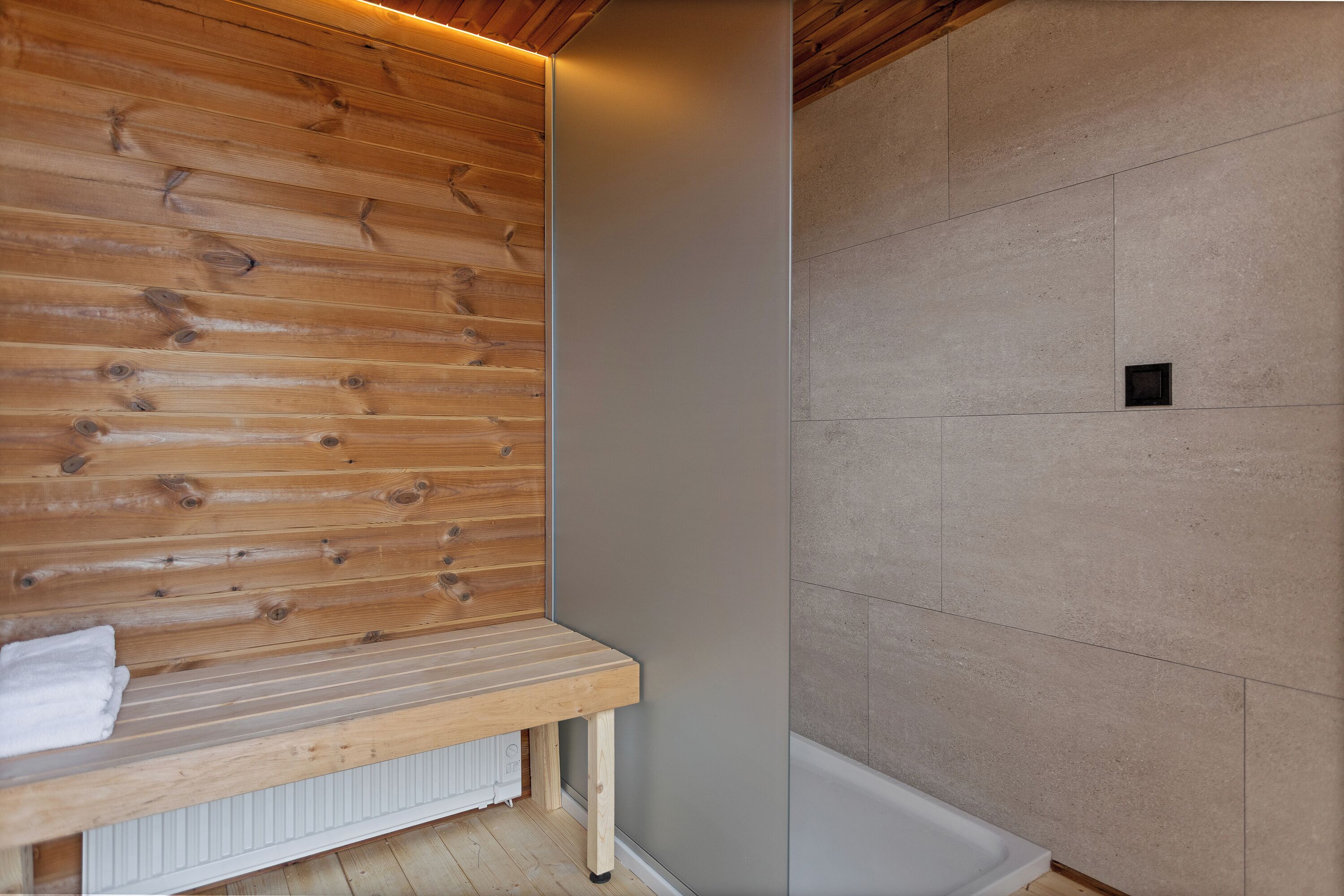 A wooden bench with a towel, a tiled wall, and a small black vent.