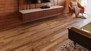 A modern living room with a large flat-screen TV mounted on a wooden wall, a wooden floor, and a cozy armchair. - Regenta Evolife Dome City Mahakumbh Prayagraj (Karchana)