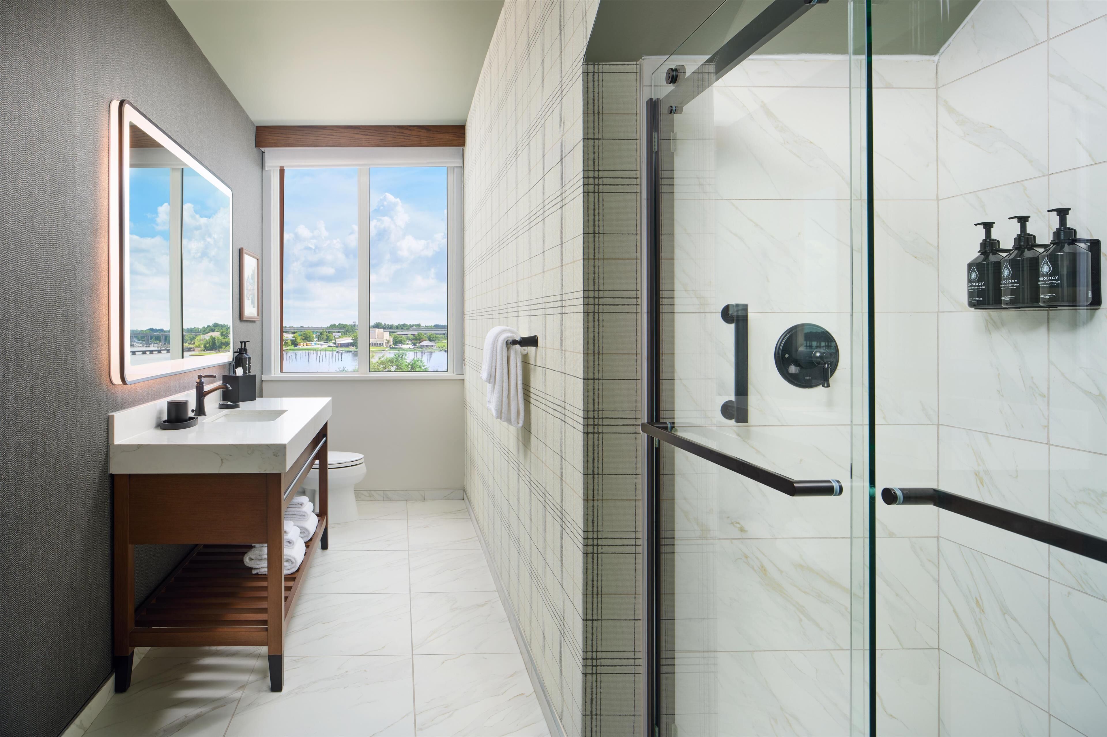 Une salle de bain moderne dotée d’une douche à parois de verre, d’un meuble-lavabo avec miroir et d’une fenêtre donnant sur l’extérieur.