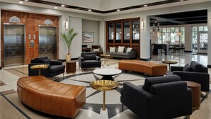 A spacious lobby with a modern design, featuring a central seating area with sofas and a coffee table, a reception desk, and a large window providing a view of the outside. - Tryon Riverfront Inn New Bern, Tapestry (New Bern)