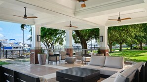 A covered outdoor seating area with modern furniture, ceiling fans, and a view of boats and greenery. - Tryon Riverfront Inn New Bern, Tapestry (New Bern)
