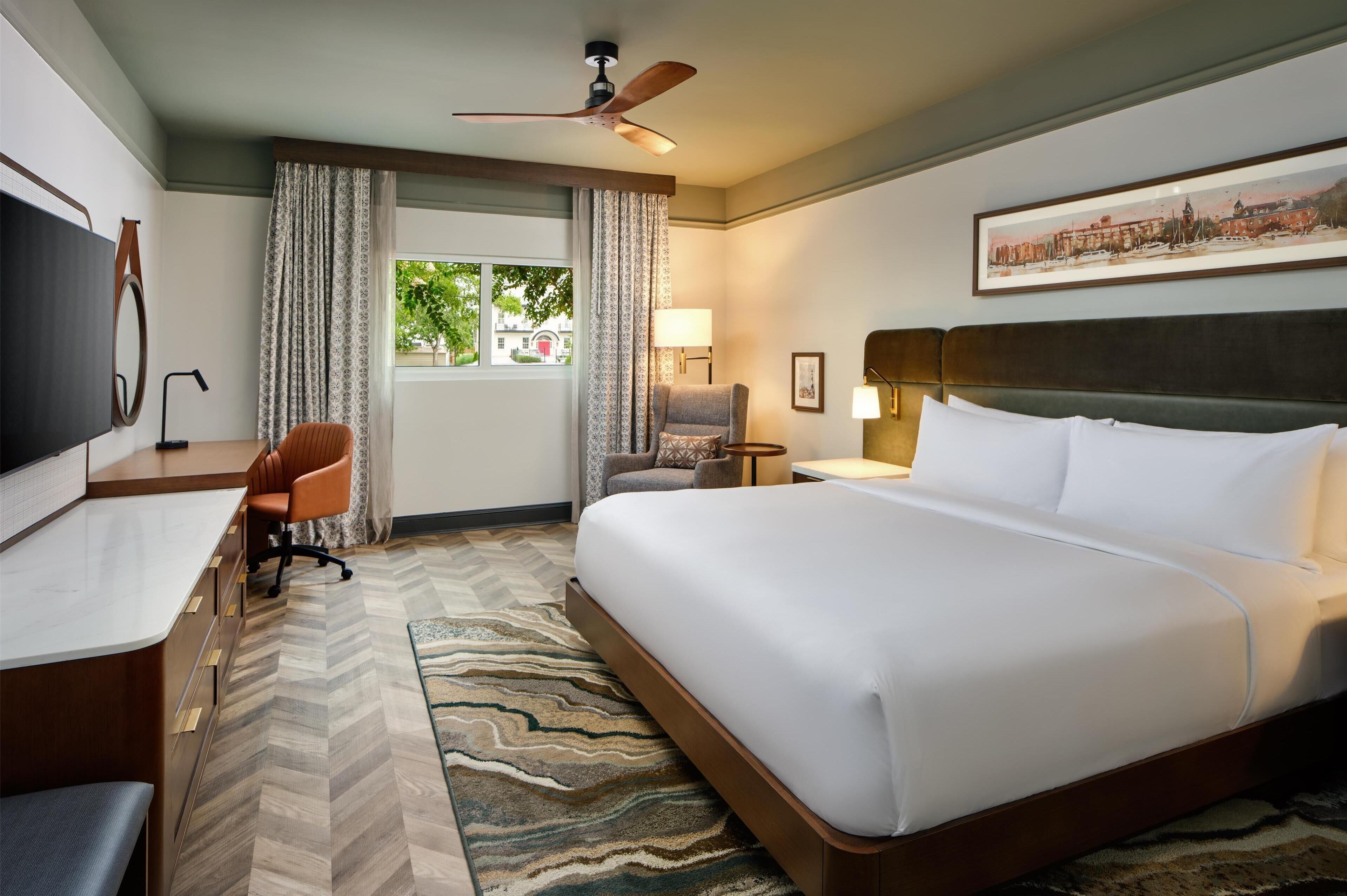 A hotel room with a bed, desk, chair, and a television.