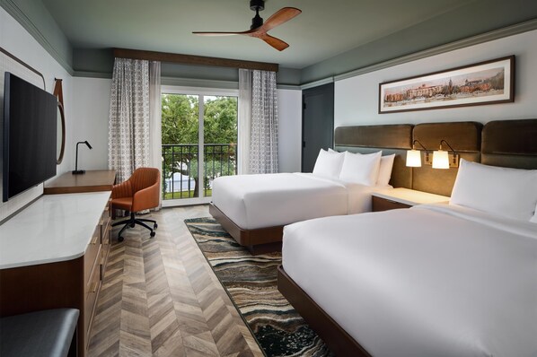 Quarto de hotel com duas camas, uma escrivaninha, uma cadeira, televisão e varanda com cortinas.
