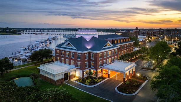 A waterfront hotel with a large building, a marina with boats, and a bridge in the background. - Tryon Riverfront Inn New Bern, Tapestry (New Bern)