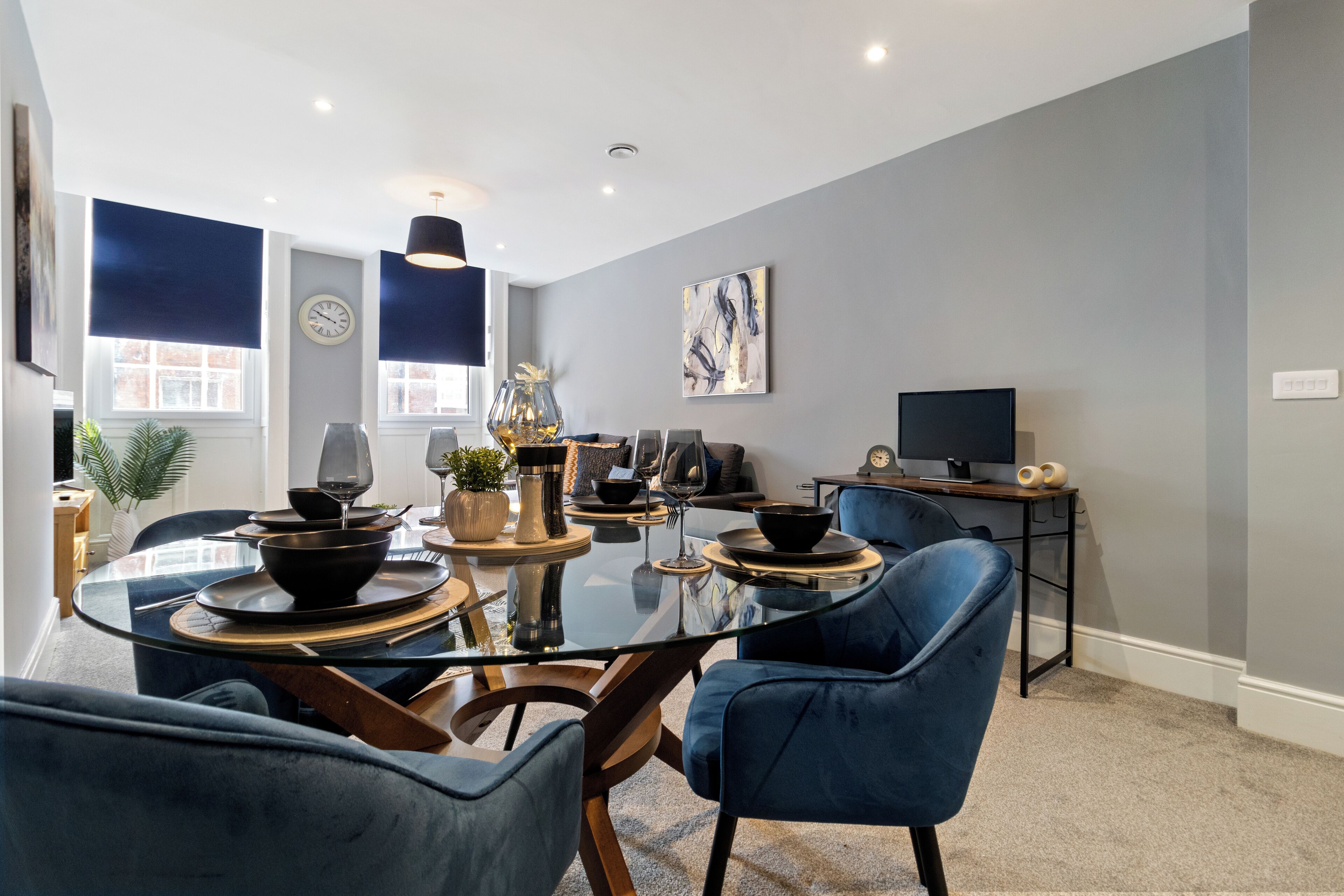 A modern dining area with a glass table, blue chairs, and a television in the background.