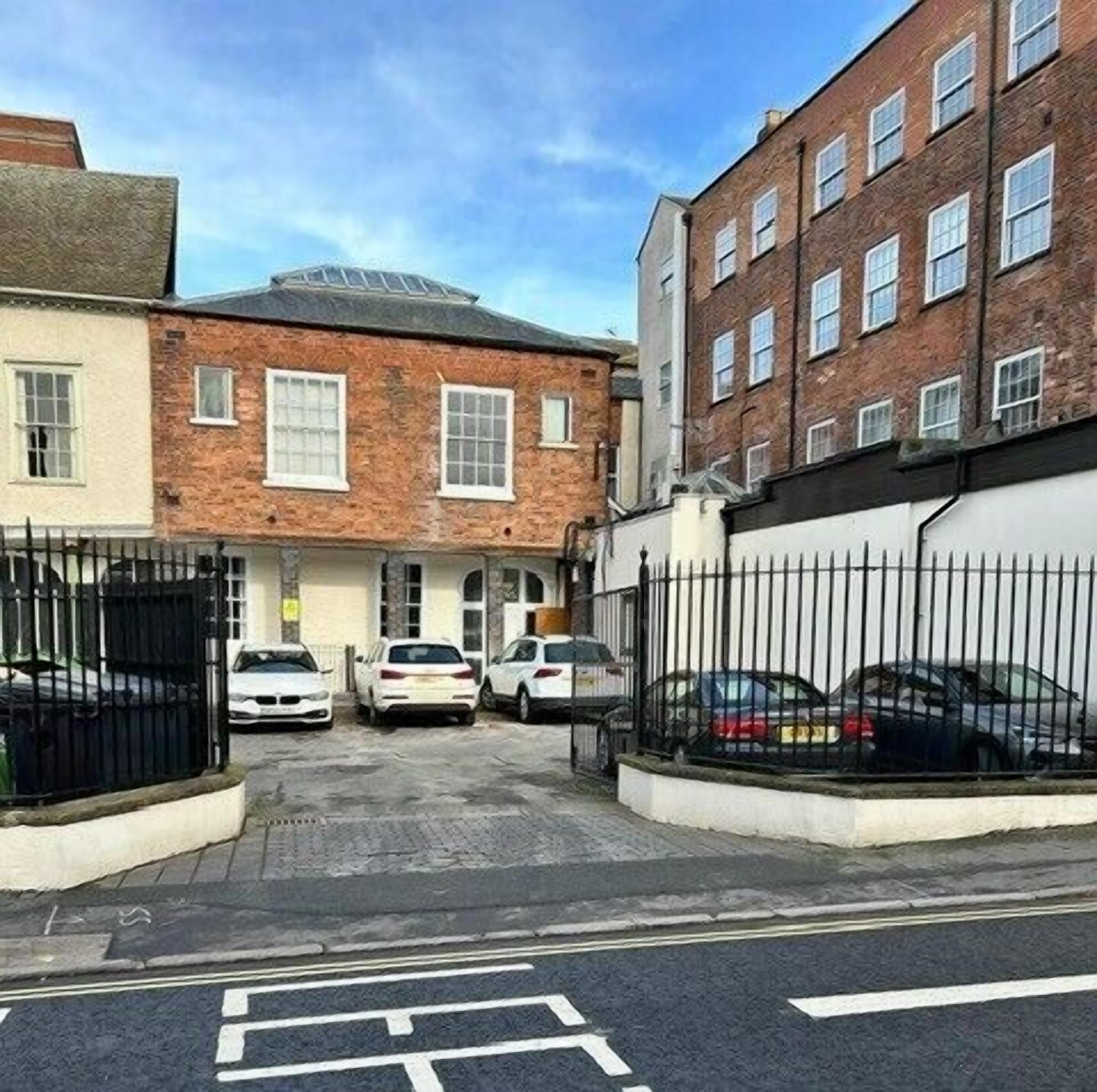 A street view with a row of parked cars, a building with brick facade, and a clear sky.