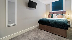 Un dormitorio con cama, un televisor de pantalla plana montado en la pared, una ventana con vistas y una mesita de noche con lámpara.