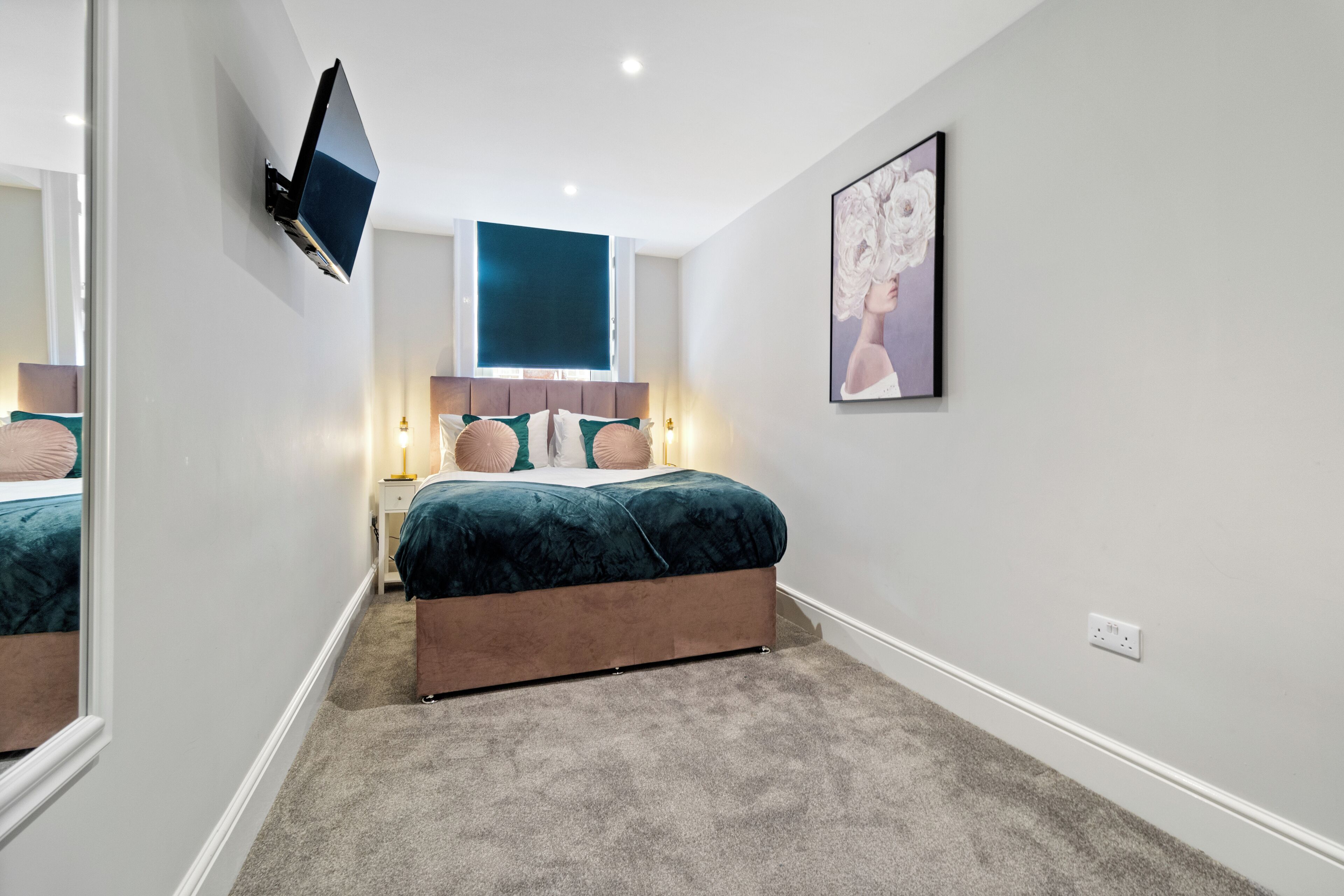 A bedroom with a bed, a mounted TV, a window, and a framed picture on the wall.
