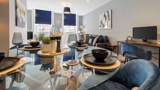 Una sala moderna con una mesa de comedor de vidrio, sofás azules y un televisor de pantalla plana.