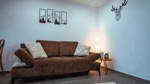 A living room with a brown sofa, a small side table, and a wall-mounted deer head decoration. - Ferienwohnungen Moselblick Bekond (Bekond)