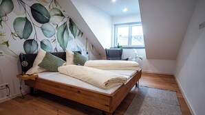 A bedroom with a wooden bed, a green and white patterned wall, a window, and a desk with a chair. - Ferienwohnungen Moselblick Bekond (Bekond)