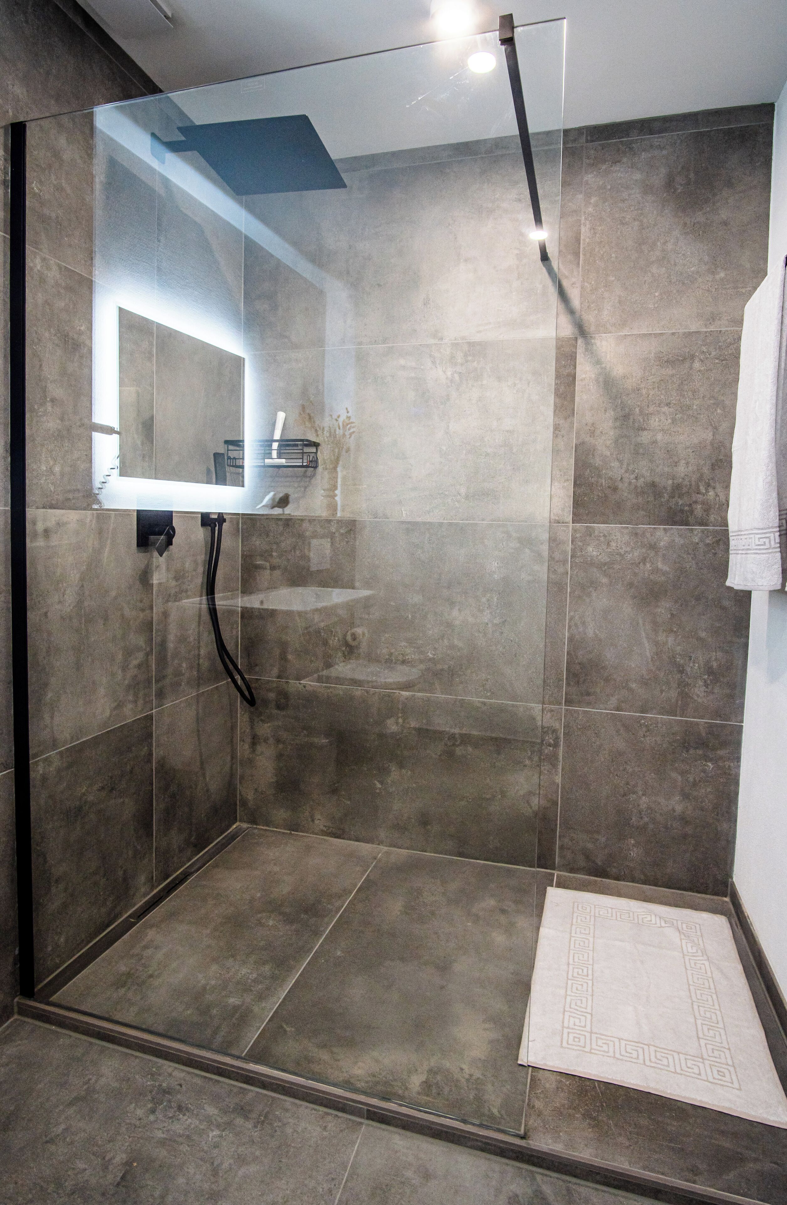 Een moderne douche met een glazen deur, een handdoekhouder en een klein plankje met toiletartikelen.