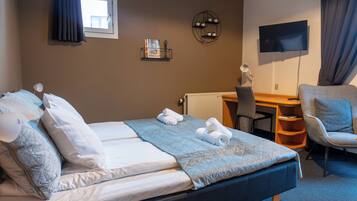 A hotel room with a bed, a desk, a chair, a TV, and a shelf with decorative items.