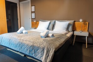 Cozy retreat with a quilted headboard and plush bedspread, featuring a nightstand with two lamps and a framed certificate.