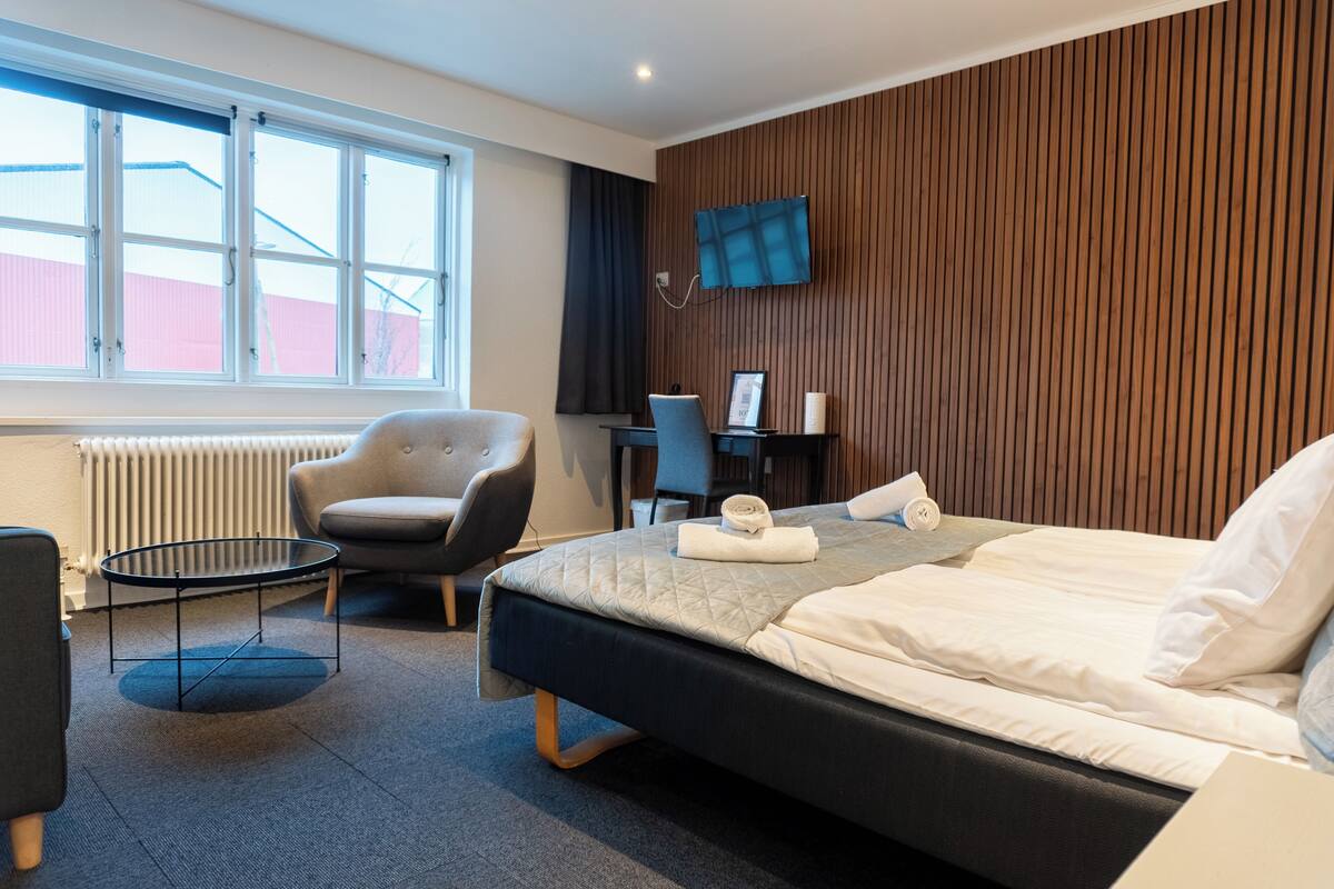 Habitación de hotel con cama, escritorio, silla y televisor en la pared.