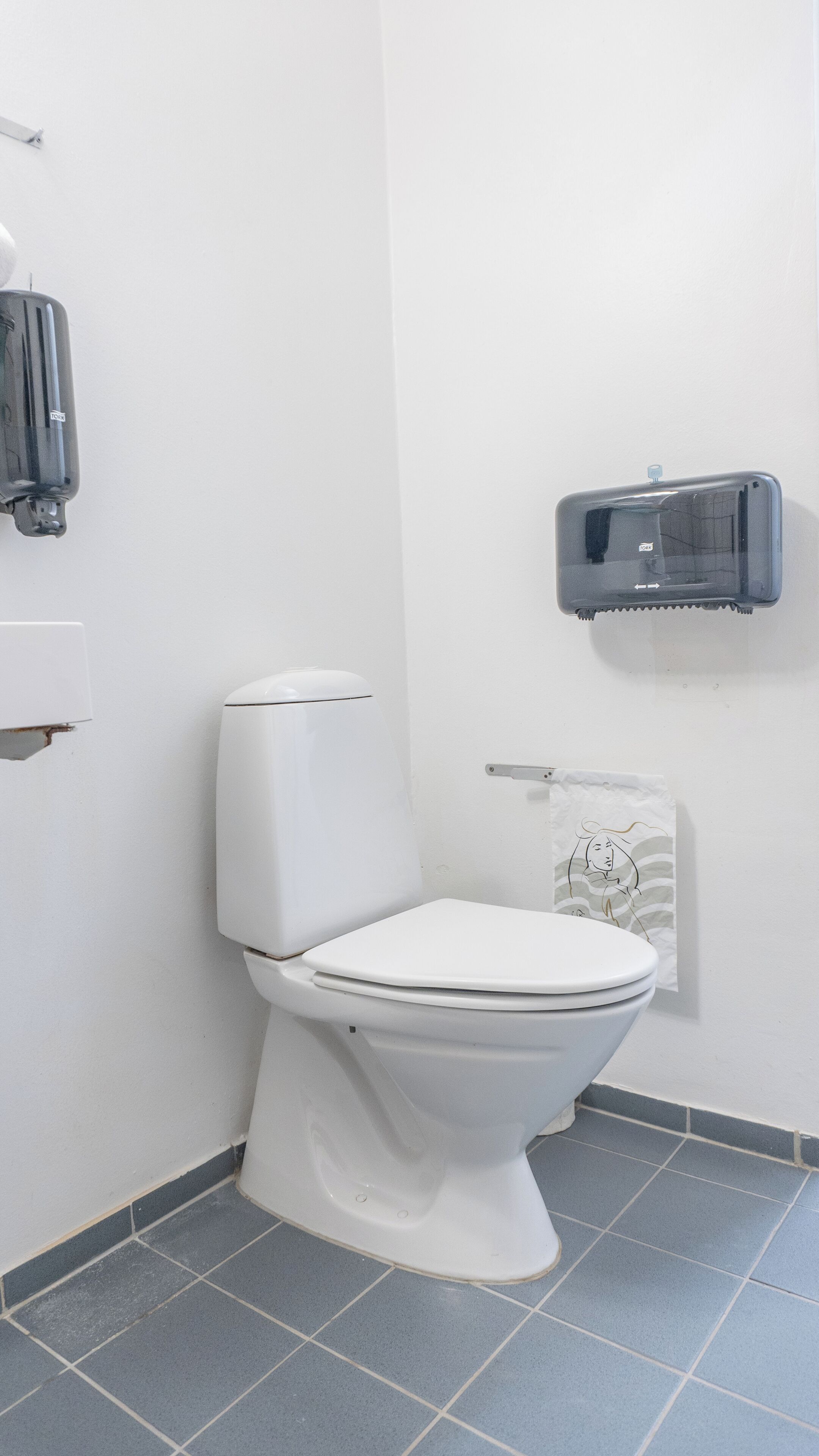 Et hvidt toilet med tank og bidétmontering på væggen.