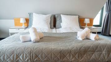 Una cama bien tendida con un cabecero acolchado, dos almohadas blancas y dos toallas enrolladas.