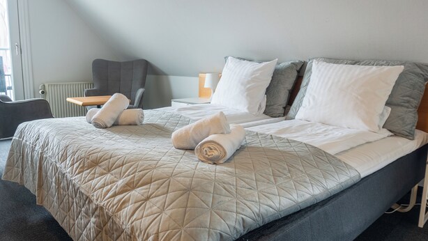 A neatly made bed with a quilted beige bedspread and two rolled towels. - Hotel Assens (Assens)