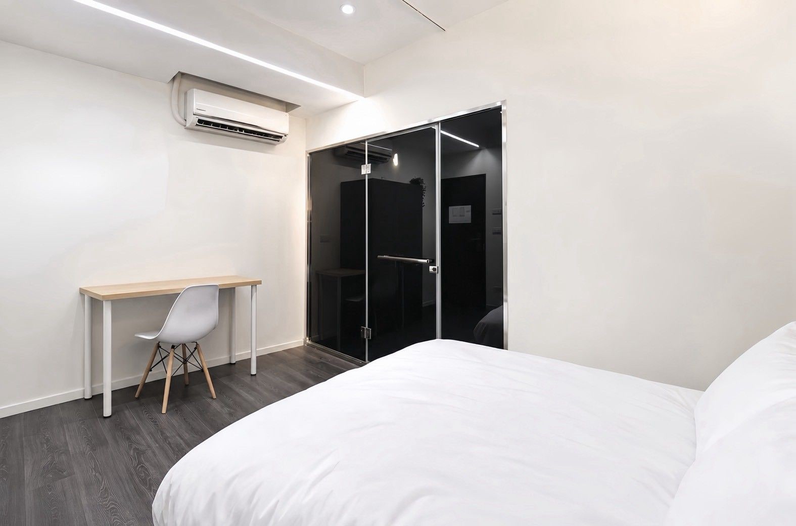 A modern hotel room with a bed, a desk, a chair, and a walk-in closet.