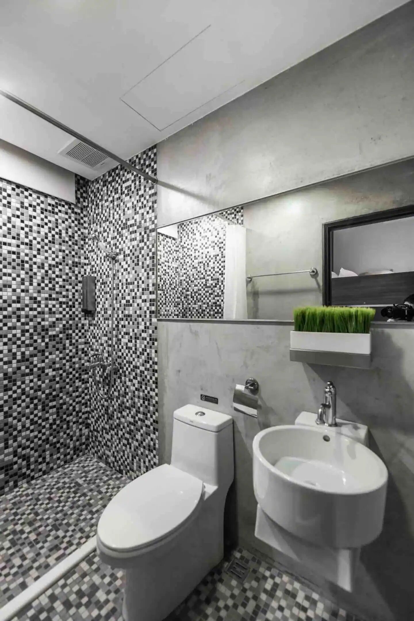 A modern bathroom with a checkered floor, a toilet, a bidet, and a mirror with a green plant.