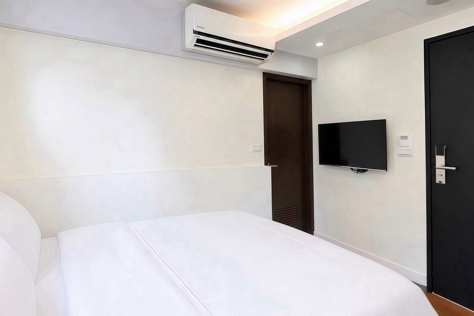 Habitación de hotel con cama, televisión montada en la pared, una puerta y un equipo de aire acondicionado.
