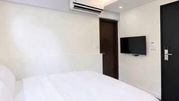 Habitación de hotel con cama, televisión montada en la pared, una puerta y un equipo de aire acondicionado.